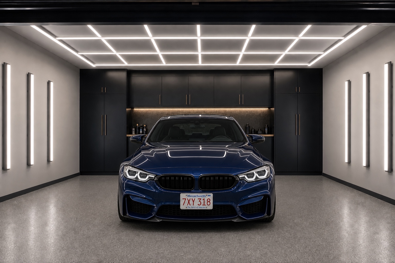 Ceiling and wall inspection lights illuminating a deep-blue performance coupe parked straight and centered with a Massachusetts plate