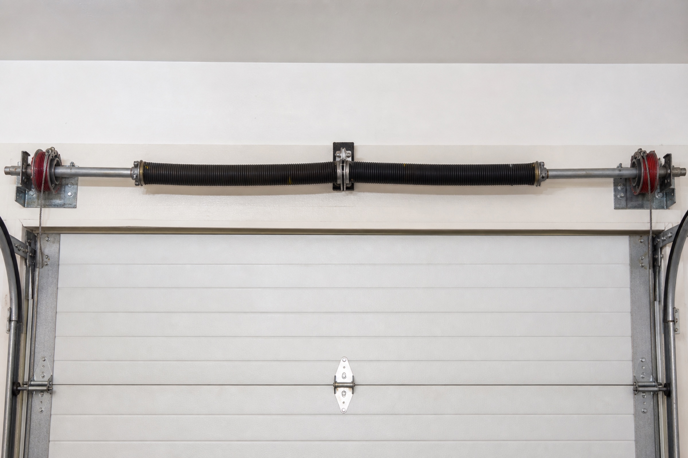 Representative residential torsion spring assembly mounted above a white sectional garage door